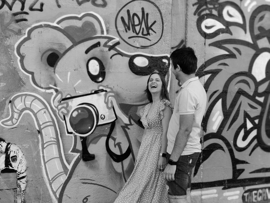Casal a rir junto a um graffiti de um rato com uma câmara