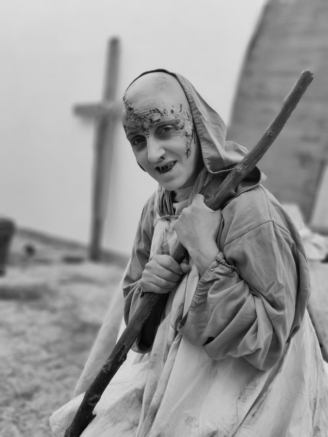 Figura mascarada com um cajado, diante de um cruzeiro